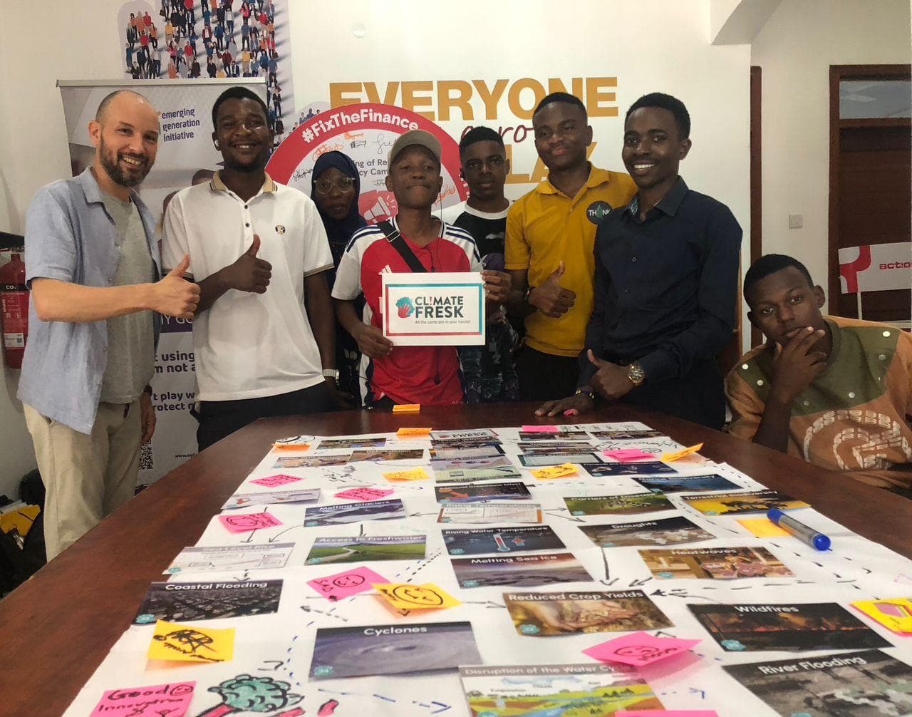 Participants and a facilitator holding certificates behind a table of climate cards.