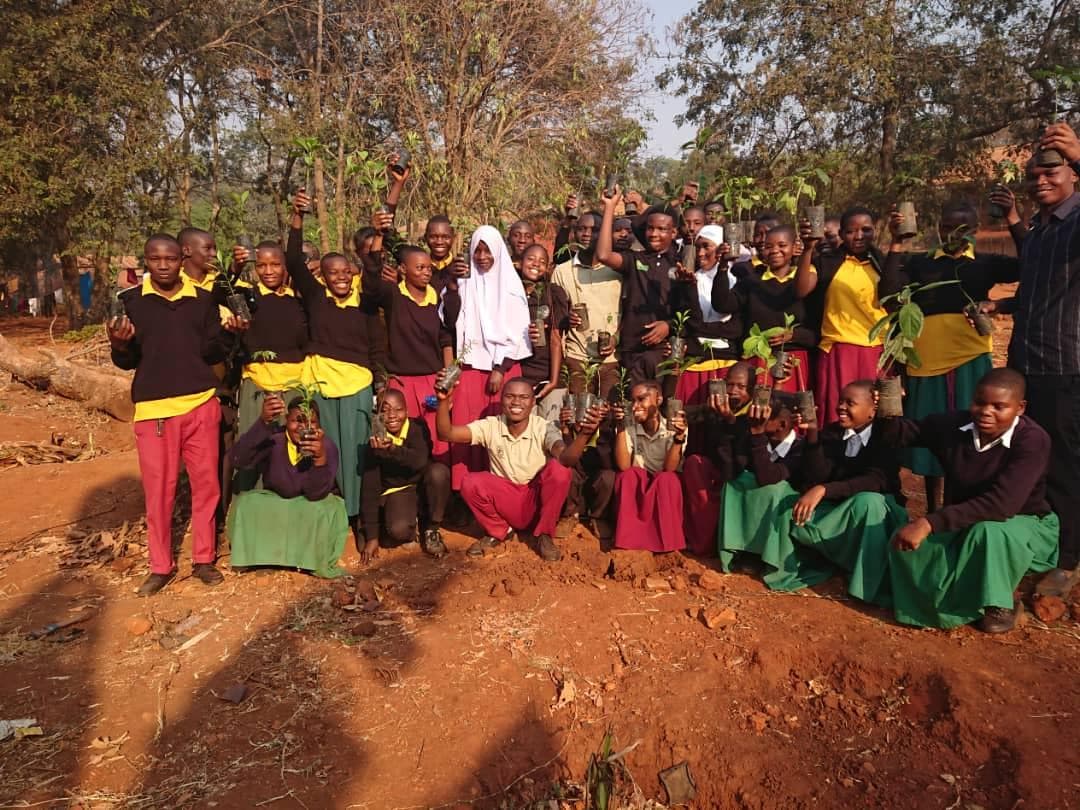 Students and environmental educators posing outdoors with young trees.