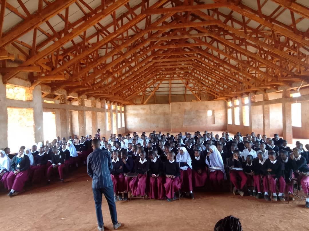 An environmental educator addressing students in a large school hall.