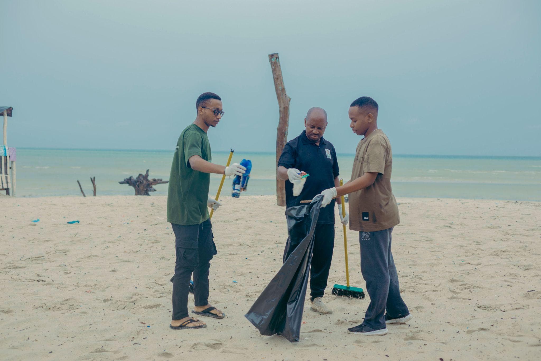 Volunteers holding an open waste bag and a cleaning tool on the beach.