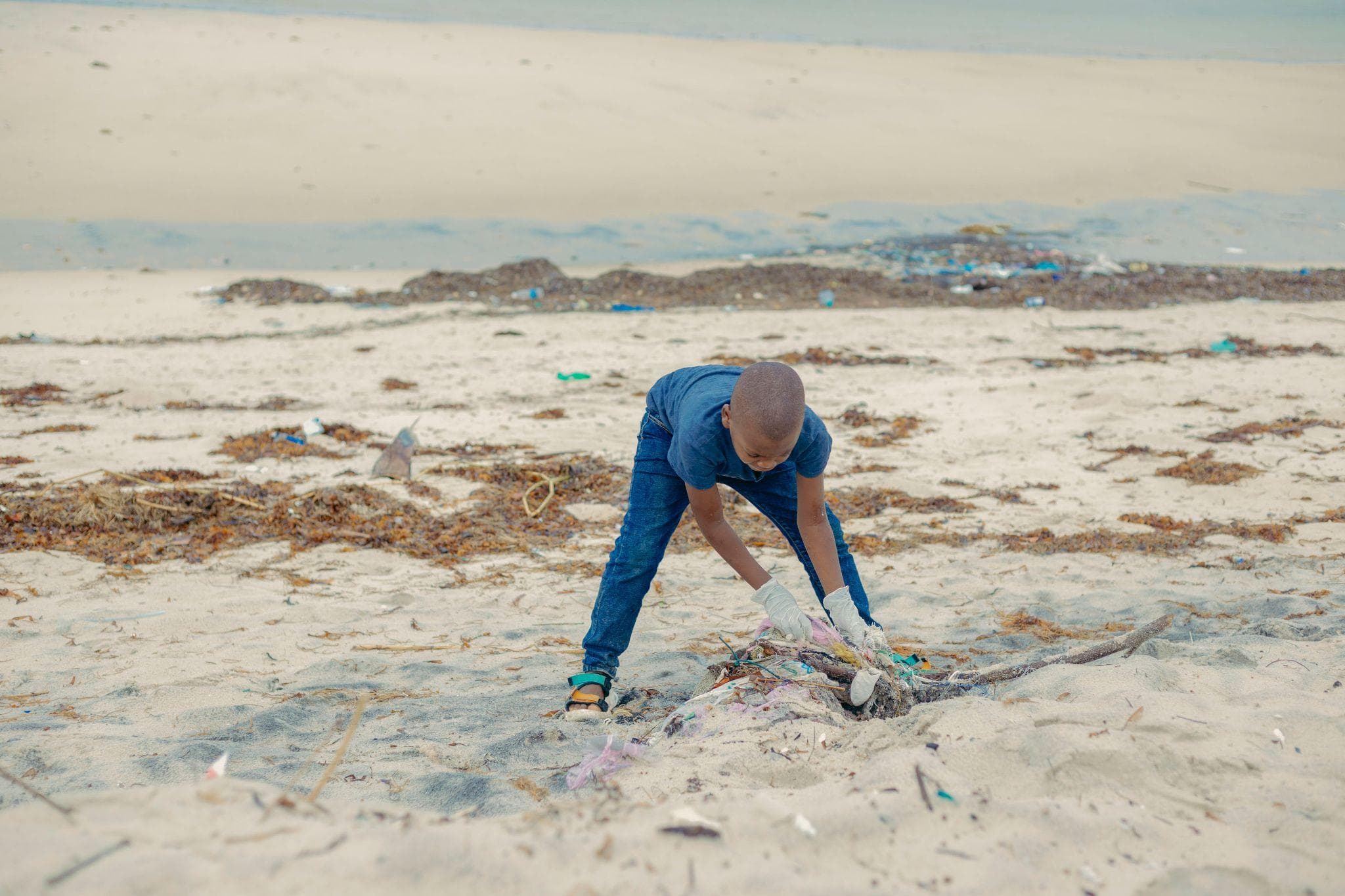 A volunteer bending down to collect litter from the sand.
